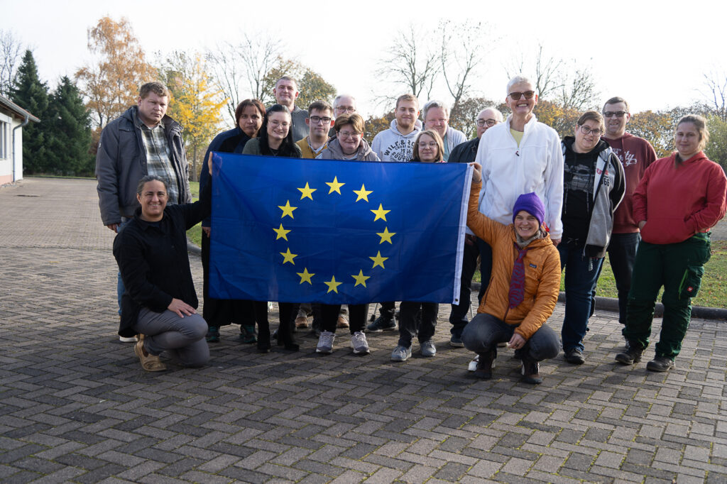 Das Bild zeigt eine Gruppe, die eine Europa Flagge vor sich hält. Sie alle lächeln in die Kamera.